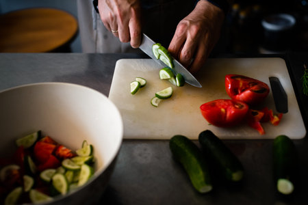 Cook cuts cucumbers for salad on a plastic board