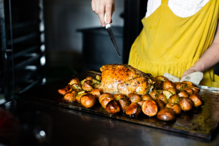 A woman cuts chicken with potatoes on a baking counter