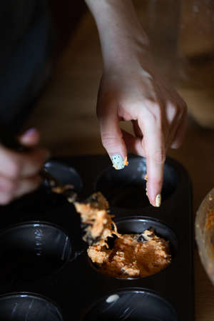 The girl spreads the dough with her finger in a muffin moldの写真素材