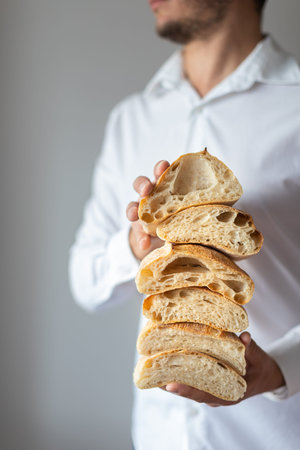 Artisan traditional bread Ciabatta in the hands of a young man on a light background. Cut into...