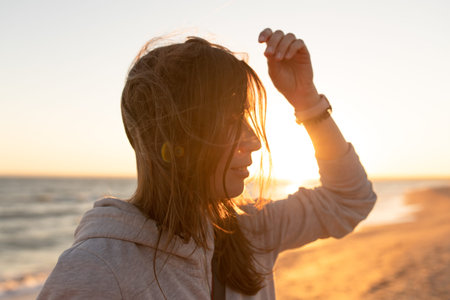 A woman at dawn or dusk corrects her hair in the backlight. Side view.