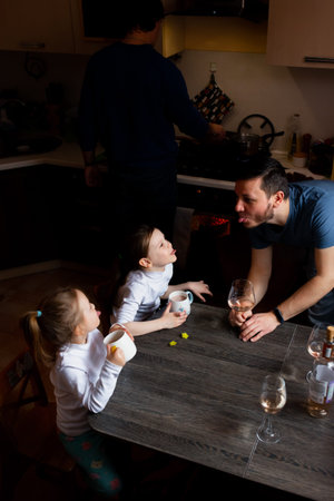 Man shows the tongue to the children, the children also show the tongue. Party family home friends. A man cooks food. Adults drink wine.の写真素材
