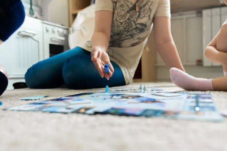 Mom and kids play a board game on the floor in the nursery, mother throws dice. Front view.の写真素材