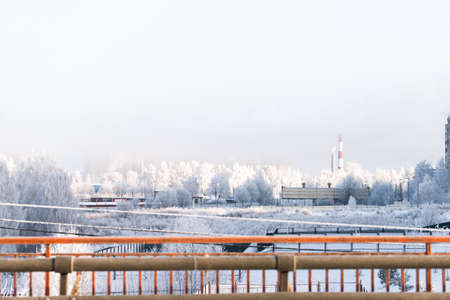 The cityscape is a frosty morning after a snowfall. Boiler room pipes, bridge, buildings, snow-covered trees. Russia, winter.の写真素材