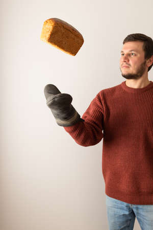 A man in a sweater throw up a loaf of rye bread into the air. Front view. Portrait.の写真素材