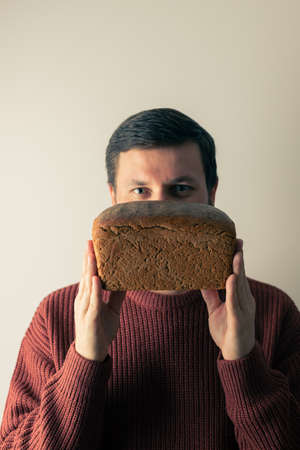 A man in a sweater holds a loaf of homemade rye bread. Front view.の写真素材
