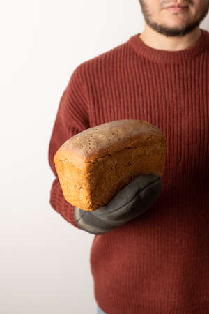 A man in a sweater holds a loaf of homemade rye bread. Front view.の写真素材