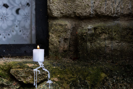 A candle burns on the windowsill of an old limestone house by the window. Front view.の写真素材