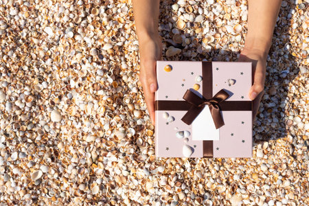 Hands hold out a gift against the background of the beach of small shells. Top view.の写真素材