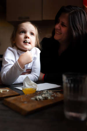 A girl eats cheese with blue mold in her mothers arms in a country house.の写真素材