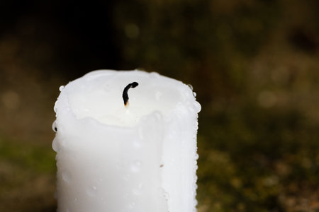 An extinguished candle after the rain. Black wick and drops of water on the wax. Front view.の写真素材
