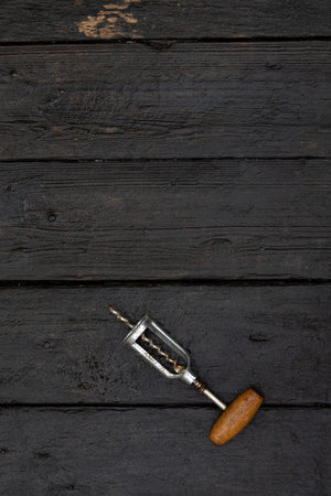 The corkscrew for opening wine lies on a dark wooden background. Top view. Flat lay.