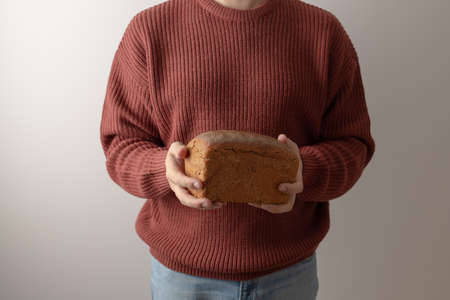 A man in a sweater holds a loaf of homemade rye bread. Front view.の写真素材