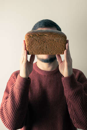 A man in a sweater holds a loaf of homemade rye bread. Front view.の写真素材