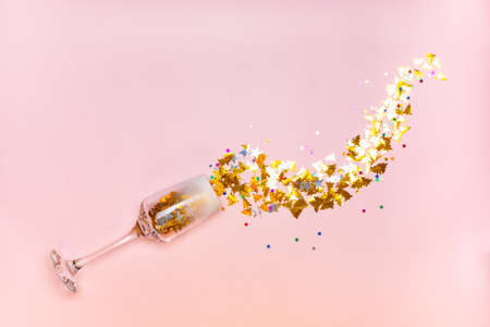 New Year card. Glass of champagne, gold sparkles in the form of Christmas trees and stars, pouring out of the glass on a pink background. Top view.の写真素材