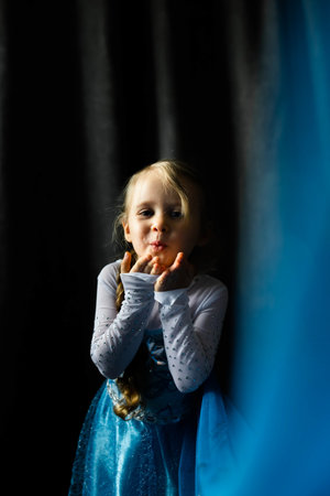 A portrait of a little girl sending an air kiss on a dark blue background. Front view.の写真素材