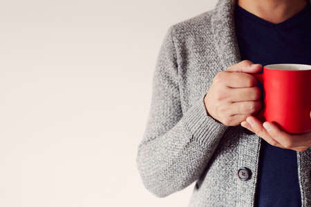 A man with a red mug of coffee in his hand wearing a cardigan. The concept of autumn. Front view. Copy space.の写真素材