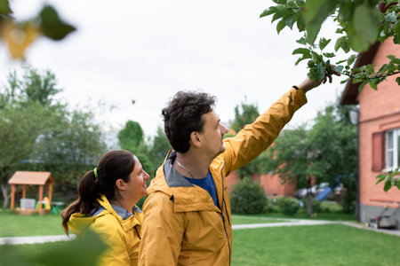 A married couple in yellow raincoats in the rain in their backyard. Front view.