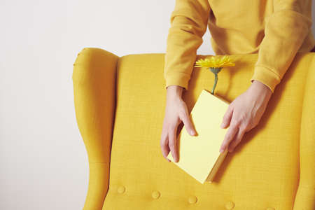 A yellow chair with a yellow book in hands in which a flower is placed. Front view.の写真素材