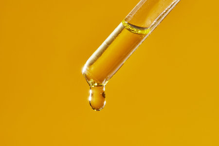 A drop of cosmetic aromatic oil drips from the pipette. Front view.