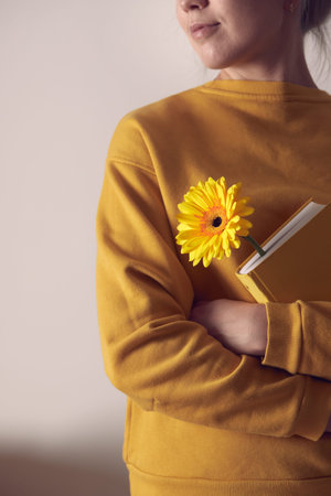 A yellow book with a flower bookmarked in the hands of a woman. Front view.