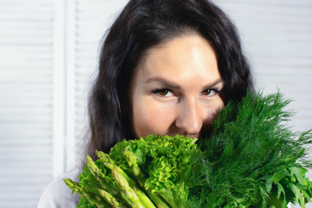 Smiling woman with salad leaves, celery and dill with parsley. Spring and vitamins. The concept of...