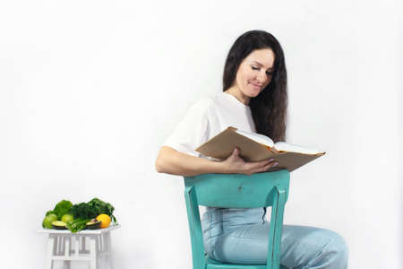 The concept of studying proper nutrition. Woman with a book, an apple and a set of vegetables and fruits. Front view.の写真素材