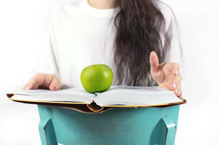 The concept of studying proper nutrition. Woman with a book, an apple and a set of vegetables and fruits. Front view.の写真素材