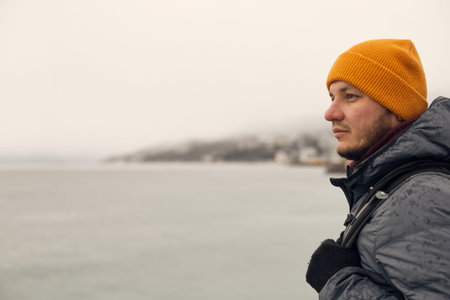 A man in winter clothes by the sea looks into the distance. The concept of travel, winter holidays....