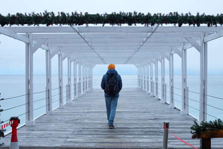 A man in winter clothes by the sea looks into the distance. The concept of travel, winter holidays. Front view.の写真素材