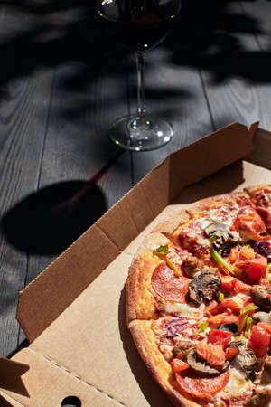 A box of pizza and a glass of wine on a summer day. Pizza delivery concept. Vertical photo.の写真素材