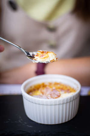 A young woman eating creme brulee outside in a restaurant, a concept of vacation and enjoying summer. Vertical photo.の写真素材