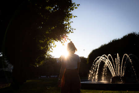 A girl against the backdrop of a sunset in a park with a fountain. St. Petersburg, Russia. Front view.の写真素材