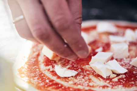 Cheese is placed on the pizza dough with sauce. The process of making homemade pizza. The concept of homemade fast food. Front view.の写真素材