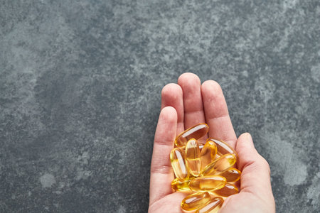 A person holds an omega-3 fatty acid capsule against a gray background. The concept of medicine and...