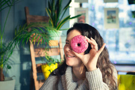 Portrait of an attractive woman in a cafe with a doughnut. Winter, warm clothes, coffee and sweets. Front view.の写真素材