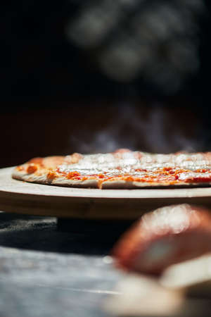 Ready-made pizza on a stand. The process of making homemade pizza. The concept of homemade fast food. Vertical photo.の写真素材