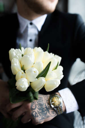 A brutal man with tattoos and a bouquet of flowers. The concept of a date. Vertical photo.の写真素材