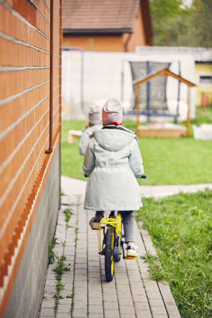 Little girls on bicycles ride around the yard. The concept of a happy childhood. Vertical photo.の写真素材