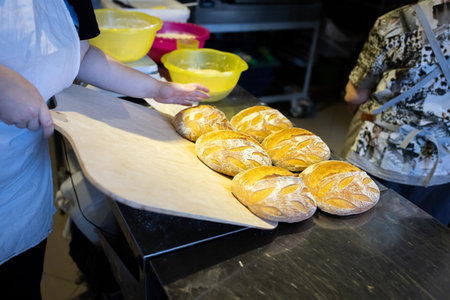 A baker unloads a finished batch of artisan wheat bread fresh from the oven with a shovel. Front...