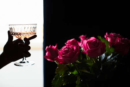 Woman holds a glass of champagne in her hand, next to it is a bouquet of flowers made of roses. The concept of a gift and congratulations. Front view.の写真素材