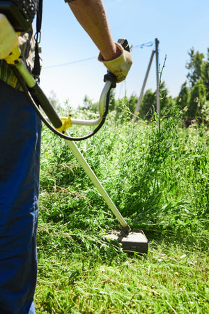 A man mows the grass in the field with a trimmer. Yard care concept. Vertical photo.