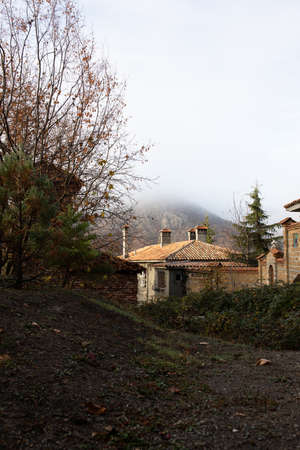 A beautiful old house in the foothills. Cozy dwelling, autumn forest and mountain fog. Vertical photo.の写真素材