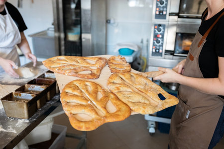 A woman in a bakery takes traditional French Fougasse bread out of the oven. Front view.の写真素材