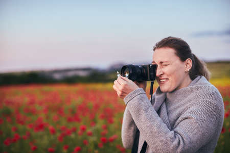 Portrait of a smiling woman in a poppy field with a camera. Front view.の写真素材