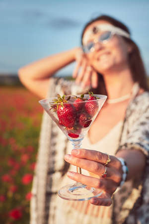 A woman eating strawberries at sunset in a field of poppies. Vertical photo.の写真素材