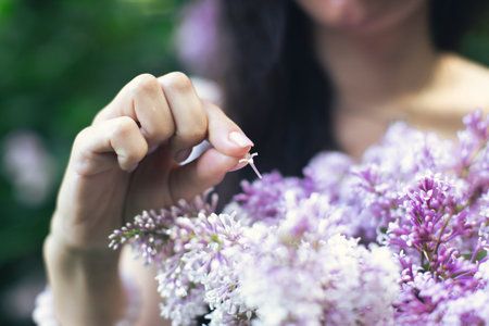 Portrait of an attractive woman surrounded by lilac bushes. Spring and summer, seasonal photos. Divination on petals. Vertical photo.の写真素材