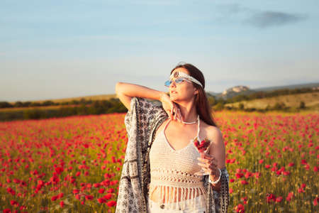 A woman eating strawberries at sunset in a field of poppies. Front view.の写真素材