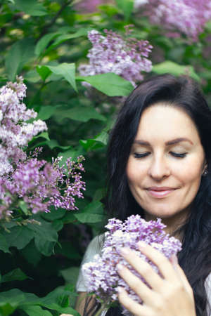 Portrait of an attractive woman surrounded by lilac bushes. Spring and summer, seasonal photos. Vertical photo.の写真素材