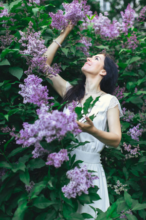 Portrait of an attractive woman surrounded by lilac bushes. Spring and summer, seasonal photos. Vertical photo.の写真素材